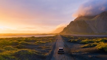 Gravel road at a golden Sunset with Vestrahorn mountain in the background and a car driving the road in Iceland Gravel road at a golden Sunset with Vestrahorn mountain in the background and a car driving the road in Iceland